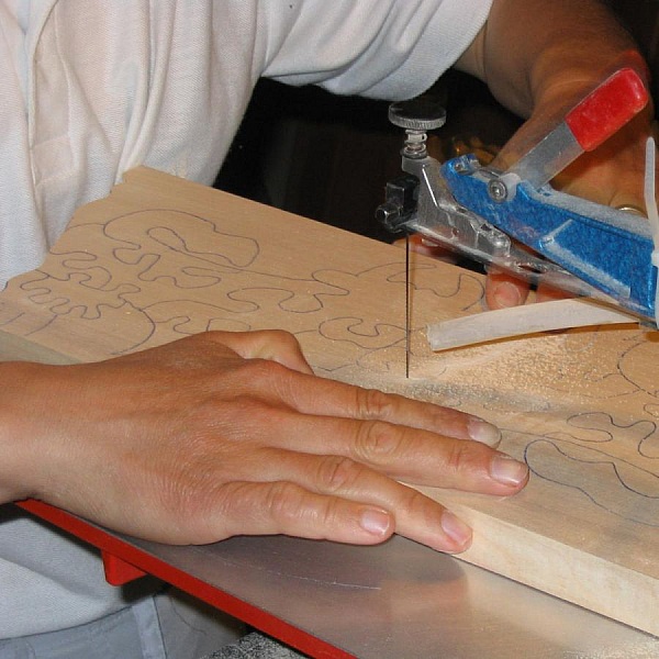 Découpe manuelle d'un puzzle en bois de hêtre à la scie.